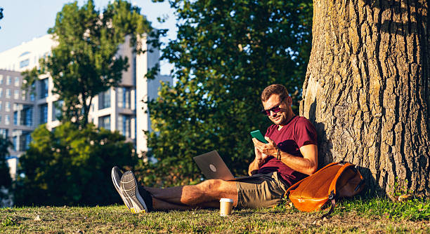 istock Man using smartphone and laptop while sitting on the ground in city park 2252312291