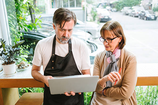 istock Cafe owner and financial advisor discussing business strategy using a laptop in a modern coffee shop. Bright setting with plants and wine bottles, symbolizing collaboration and entrepreneurship. 2252317208