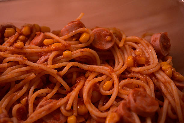 Close-up of a homemade meal consisting of spaghetti, corn, sliced ​​sausage, and tomato sauce.