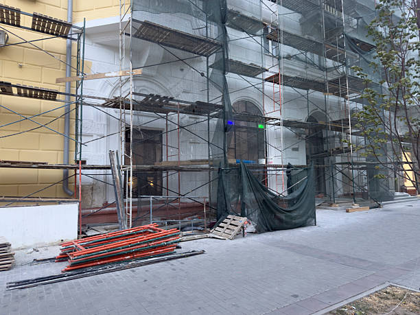 Workers prepare building materials at a construction site with scaffolding and tools in the evening.