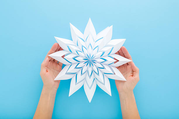 istock Woman hands holding and showing white snowflake shape from paper on light blue table background. Pastel color. Making decoration element for winter festive. Closeup. Point of view shot. Top down view. 2252325231