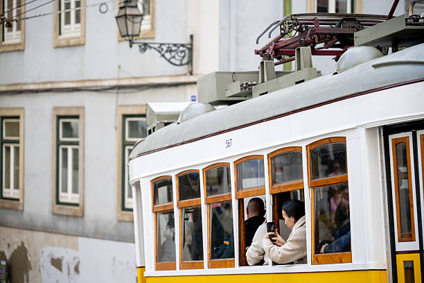 Lisbon Portugal December 05 2025. Passengers ride inside a historic yellow tram traveling through a narrow residential street in Alfama.