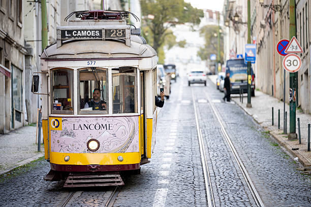 Lisbon Portugal December 05 2025. A historic yellow tram approaches along a cobblestone street with passengers visible inside.