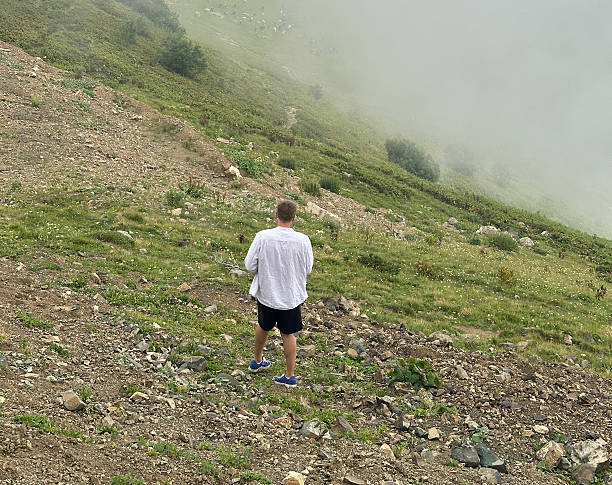 A person explores a misty mountain trail surrounded by greenery and rocky terrain.