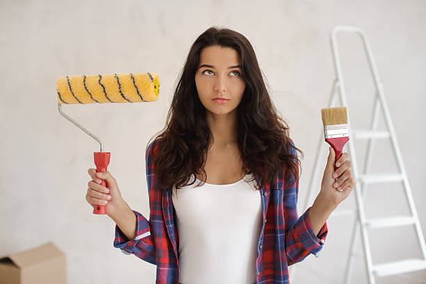 istock Thoughtful Woman Holding Paint Roller and Brush for DIY Home Makeover 2252340421