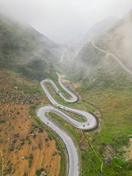 defaultHigh-altitude view of twisting Ha Giang Loop road with cyclists and motorbikes moving through steep mountains.