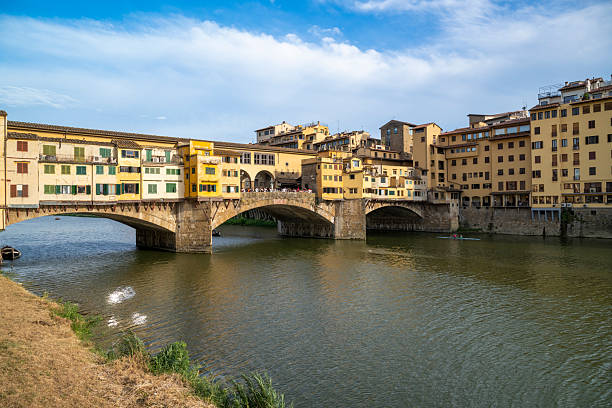 Scenic view of a famous Ponte Vecchio stone bridge with arches and pastel buildings reflected in the river, capturing timeless Italian cityscape charm, tourism appeal, and historic atmosphere in Florence, Italy.