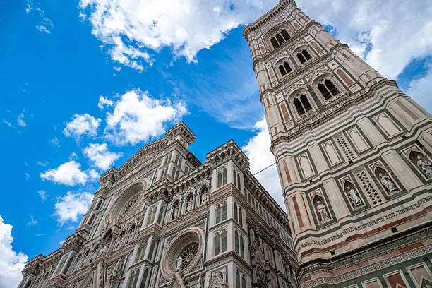 Low-angle view of Florence cathedral facade and Giotto’s bell tower against a vivid blue sky, highlighting ornate marble patterns, Gothic details, and monumental Italian architecture in the historic city center.
