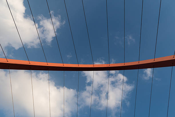 Minimalistic close up of a modern bridge structure against a vibrant blue sky. The image highlights the structural details of the bridge cables and steel elements, emphasizing clean lines and contemporary design. Suitable for urban design projects, presentations, or minimalist background use.