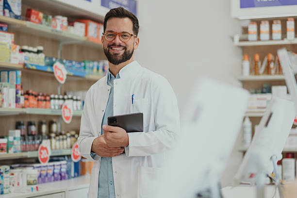 istock Smiling male pharmacist wearing lab coat holding tablet 2252355963