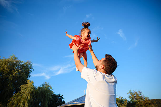 Dad and child playing in garden, backyard or park for fun. Family, father and girl with hands on face with smile, happiness and game by flowers in spring for bonding