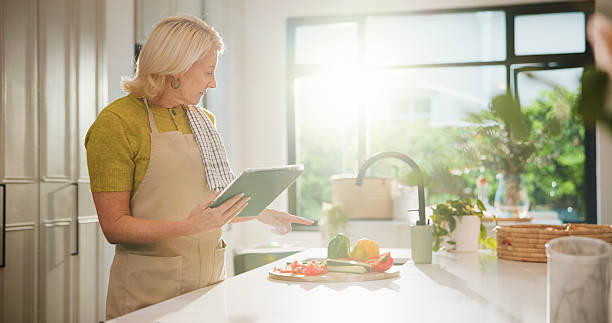 istock Senior, woman and cooking with tablet for online tutorial, healthy recipe or tips in kitchen. Elderly, female person or flare with technology or ingredients for natural organic food or meal prep 2252357261