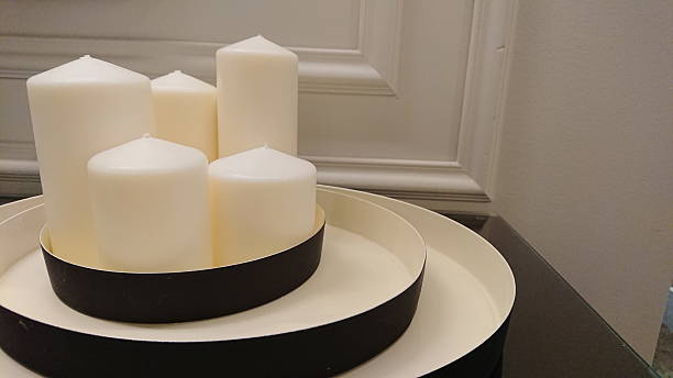 White pillar candles arranged on layered modern trays against neutral wall background. Minimalist home decor and cozy interior concept.