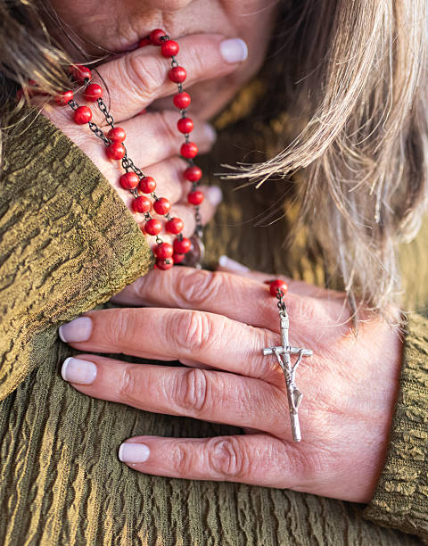 Close-up of mature woman's hands with white manicure gently holding a red rosary and crucifix, conveying faith, devotion, hope and quiet spiritual reflection in a church setting