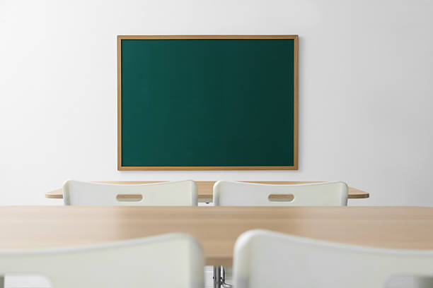 Blank green chalkboard, desks and chairs in classroom