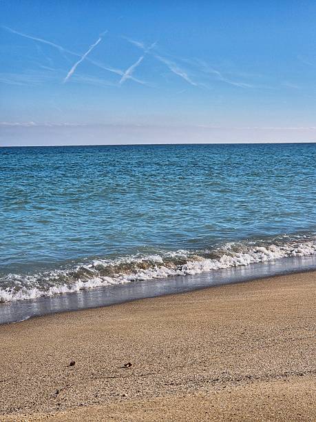istock Scenic seascape with surfline, sandy shore and blue sky with characteristic inversion trails of airplanes 2252362924