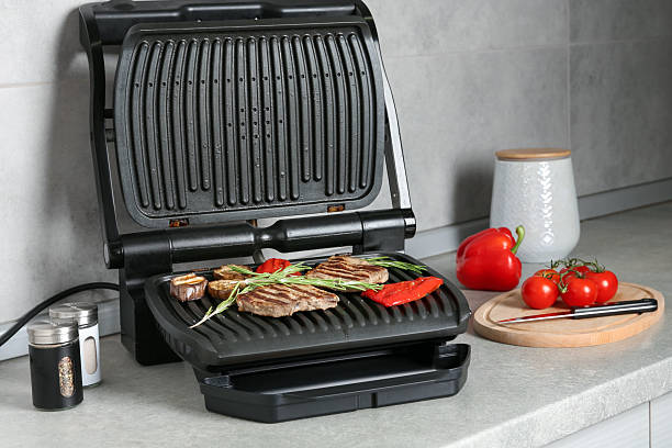 istock Open electric grill with beef steaks, rosemary, vegetables and spices on light grey table, closeup 2252364393