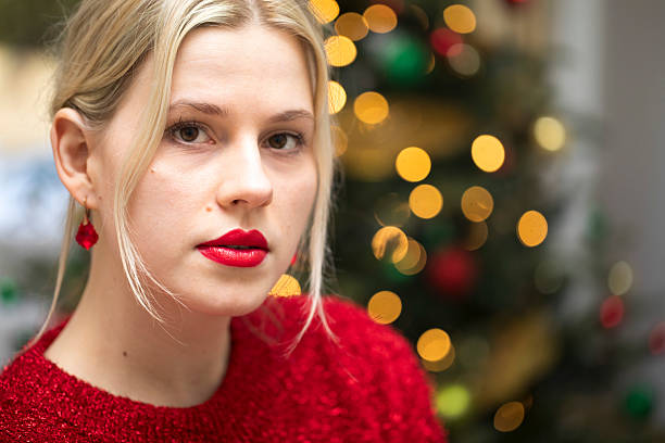 Headshot portrait of an attractive woman at home at Christmas time. She has blonde hair and is wearing a red jumper, red lipstick, and red earrings.