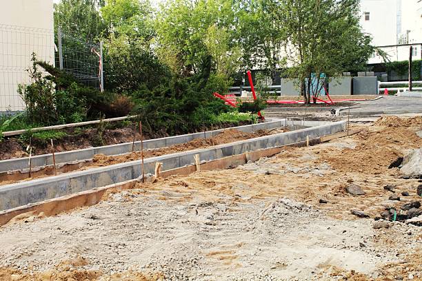 istock Curb stone installation preparation on a sunny urban construction site with wooden forms, loose dirt, gravel and nearby trees and green shrubs 2252367135