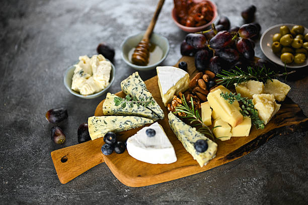 Assorted cheeses on a wooden cutting Board. Camembert, brie, Parmesan and blue cheese with grapes and walnuts. White background. Top view.