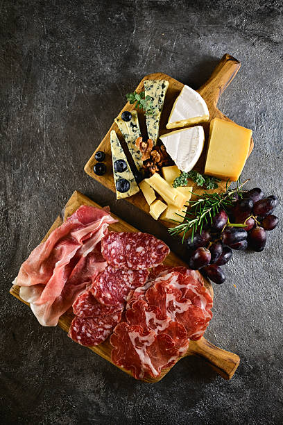 Assortment of gourmet cured meats, cheeses, grapes, and nuts arranged on rustic wooden boards