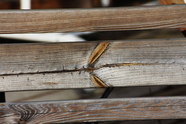A detailed view of aged wooden planks arranged diagonally, featuring cracked surfaces and peeling red paint. The texture emphasizes natural weathering and timeworn materials. Ideal for backgrounds, rustic design themes, or material surface references. No people present.