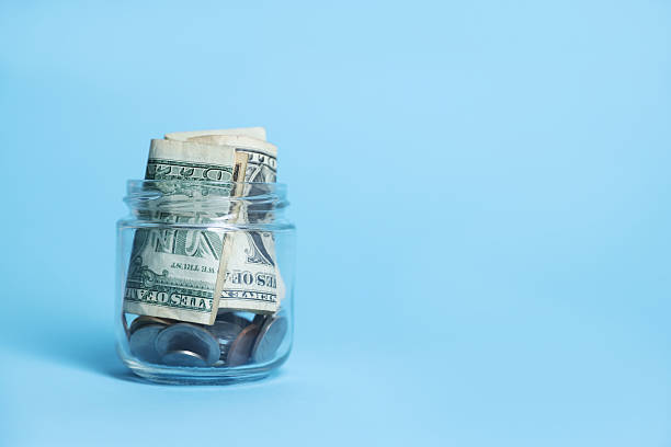 istock Glass jar with coins and dollars on light blue background, closeup. Space for text 2252376940