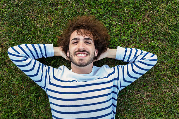istock Young man relaxing on grass with arms behind head 2252380033