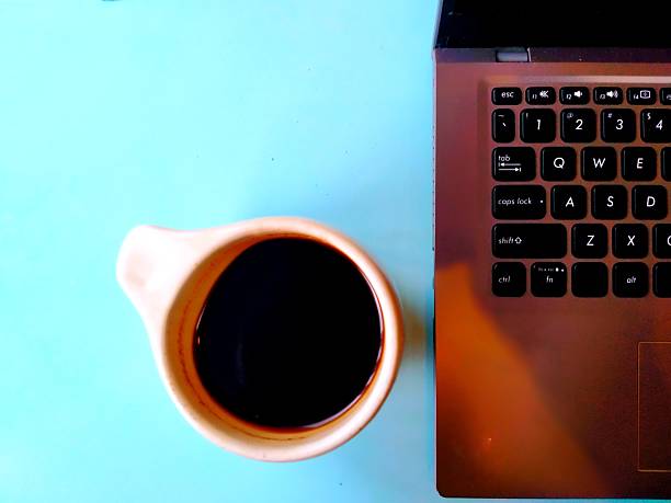 A cup of black coffee next to a laptop keyboard, placed on a light-colored work desk