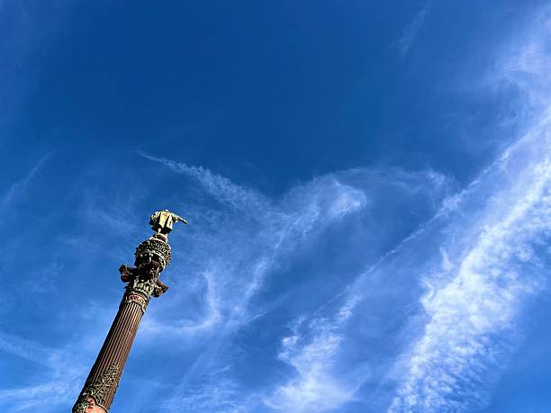 Barcelona, Cataluña, Spain - October 24, 2025: Statue of Christopher Columbus standing atop the Columbus Monument, reaching towards the sea under a vibrant blue sky with wispy clouds, symbolizing exploration, travel, and historical landmarks