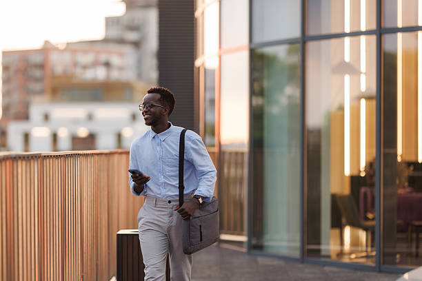 istock Young man walking outdoors in urban setting using smartphone and carrying shoulder bag 2252385540