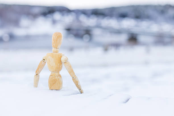 A wooden figure is standing in the snow. The scene is quiet and peaceful, with the snow covering the ground and the figure standing alone. Concept of solitude and stillness
