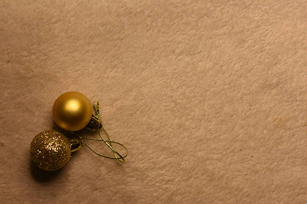 Two gold Christmas ornaments lying in the corner on a light blanket. Minimalist holiday scene with copy space.