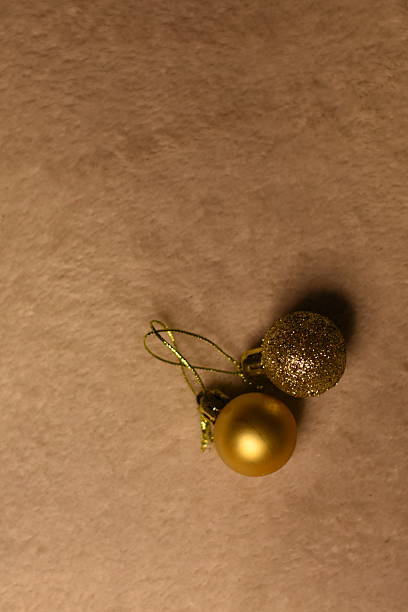 Two gold Christmas baubles lying together in the corner on a light blanket. Holiday composition with copy space.