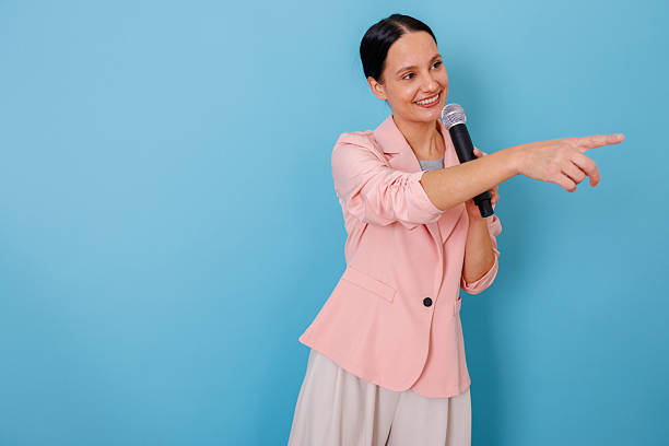 istock Woman speaker pointing while holding microphone giving business presentation or public speech on blue background 2252391732