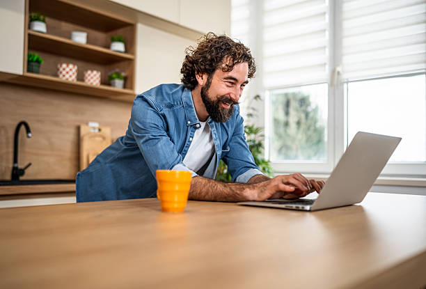 istock Man smiling working on laptop in modern kitchen 2252416175