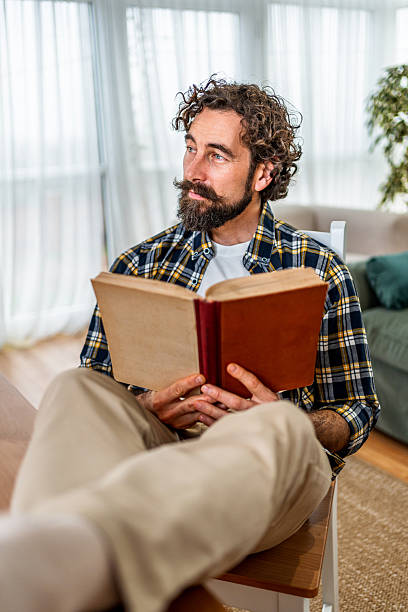 istock Thoughtful man reading book relaxing at home 2252416518