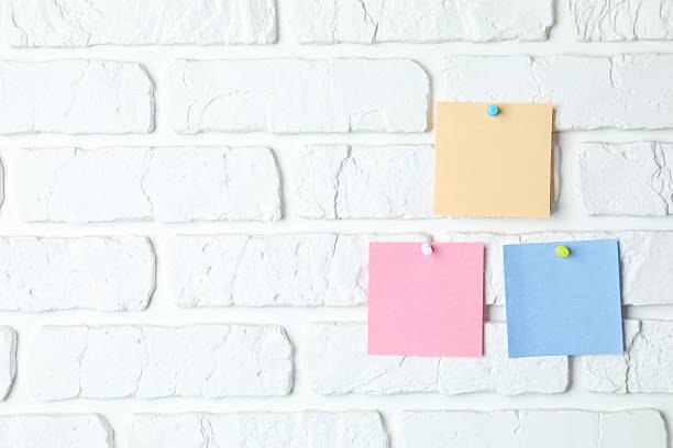 istock Colored paper stickers attached with pushpin on a white brick wall 2252424299