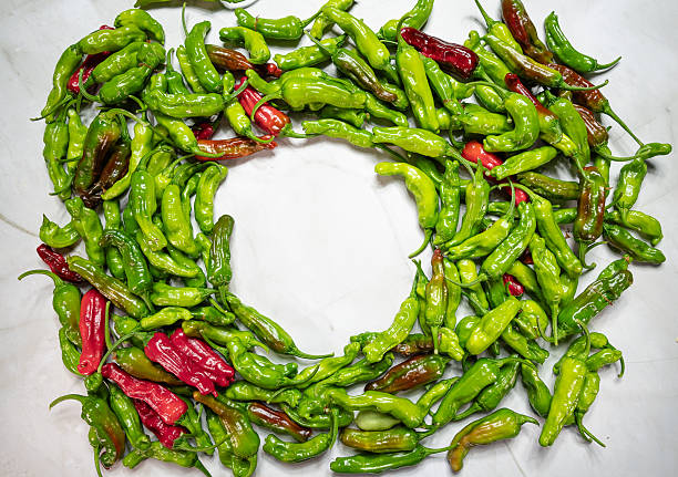 A circle of fresh, raw, shiny, spicy green and red shishito peppers with the stems still attached, lying on a plain white background.