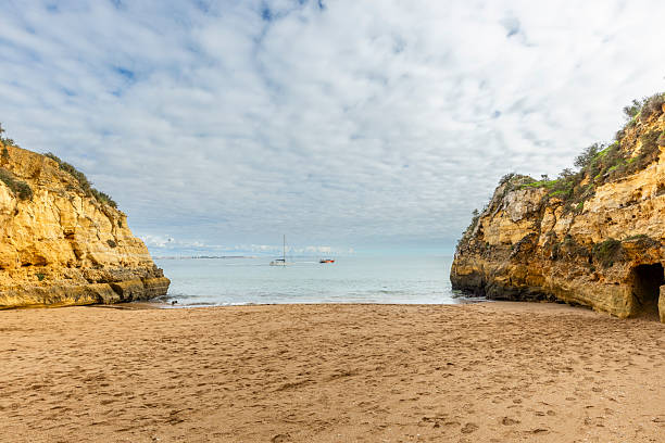Peaceful view of Praia dos Estudantes in Lagos, Algarve, Portugal, showing a golden sandy beach framed by dramatic limestone cliffs and calm Atlantic waters.