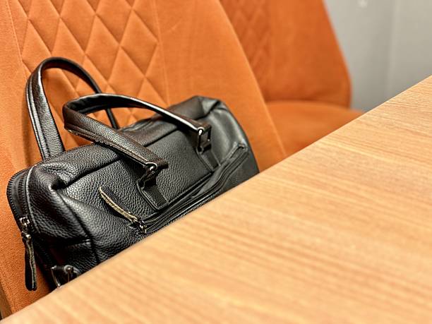 Black Leather Briefcase On Seat, CloseUp Detail Showing Grain And Zipper, Dual Handles And Shoulder Strap, Warm Orange Leather Upholstery Backdrop, TravelReady Energy, Digital Nomad