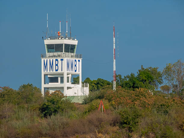Huatulco, Oaxaca, Mexico. Dec 17, 2025. A white aviation control tower with blue MMBT lettering stands above lush tropical greenery under a clear sky in Bahias de Huatulco.