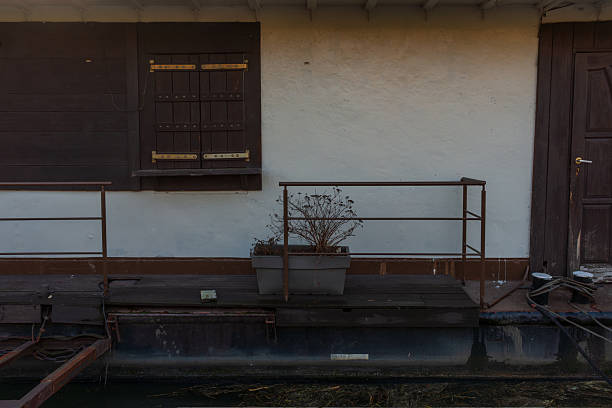 Krakow, Poland – December 13, 2025: Rustic houseboat or riverside structure detail featuring a shuttered window, dark wooden door, railing, and a planter box on a narrow deck. Minimal composition, aged materials, and calm waterfront atmosphere for architecture and texture use.