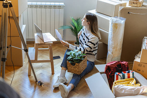 istock Young woman reviewing documents in a room with boxes during move 2252429557