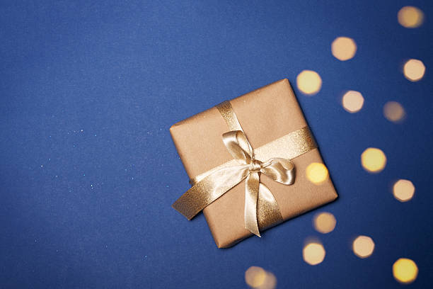 istock Gift box wrapped in craft paper with a gold bow on a blue background. 2252431234