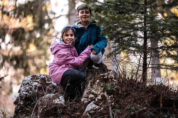 Children enjoying nature, smiling together on rocks in the forest. Exploring outdoors, healthy lifestyle and childhood memories
