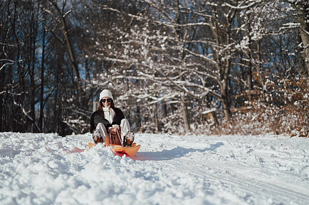 Young woman smiling while sledding down a snowy hill in a winter forest