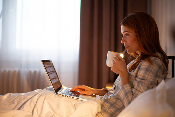 istock Woman drinking coffee using laptop in bed 2252444285