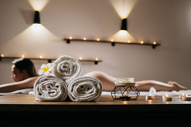 Relaxing spa setting featuring rolled towels, candles, and a serene atmosphere, with a woman enjoying a massage, embodying tranquility and self-care in a wellness retreat