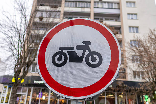 A red and white sign with a motorcycle on it. The sign is on a pole. The sign is in front of a building